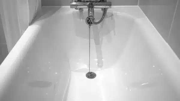 Grayscale image of an empty bathtub with a central drain plug and an attached chain, under a wall-mounted faucet.