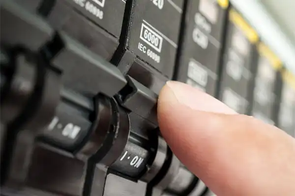 A hand is shown flipping a switch on a close-up view of an electrical circuit breaker panel.