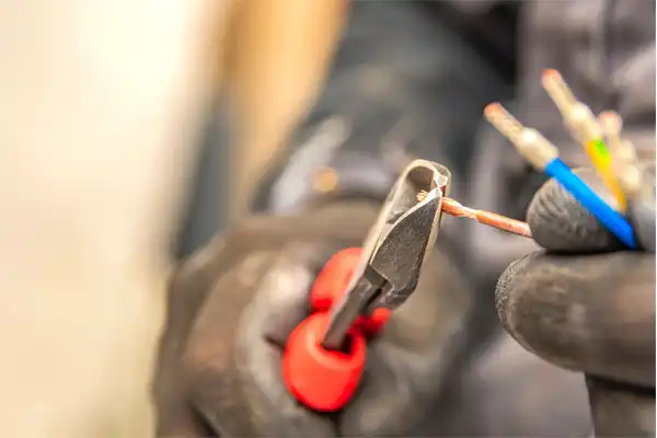 A person wearing gloves uses red-handled wire cutters to trim electrical wires.